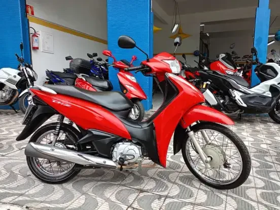 Imagem de uma Honda Biz 110i vermelha em loja de motocicletas, destaque para sua estrutura compacta e preço acessível até 15 mil reais.