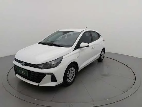 Imagem de um Hyundai HB20 branco exibido em uma plataforma circular de showroom, evidenciando seu design moderno, linhas elegantes e características do carro compacto.