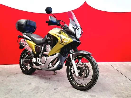 Imagem de uma moto Honda XL 700V Transalp com detalhes em amarelo e preto, equipada com baú de armazenamento na traseira, ideal para aventuras e viagens de longa distância.