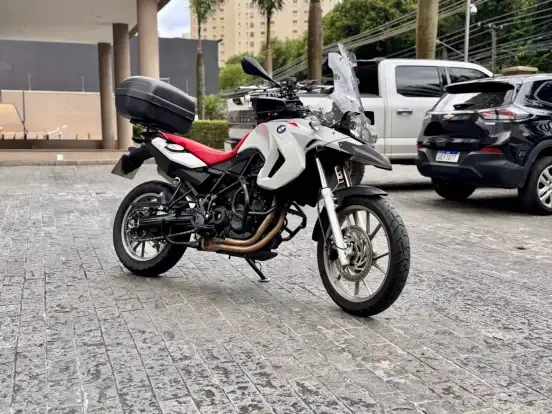 BMW F 650 GS de motocicleta em estacionamento urbano, colorida com banco vermelho e top case, ideal para aventuras off-road e viagens. Câmera capturando detalhes do visual robusto.