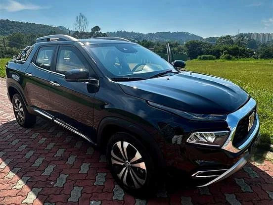 Carro FIAT Toro preto, SUV moderna com design robusto, estacionamento ao ar livre, fundo de natureza com árvores e céu claro.