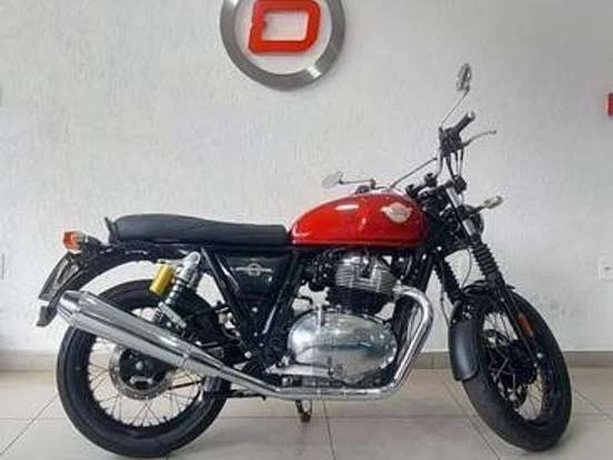 Imagem de uma motocicleta Royal Enfield Interceptor vermelha e preta exibida em uma loja, destacando sua estrutura clássica, design retro e performance até 60 mil reais.